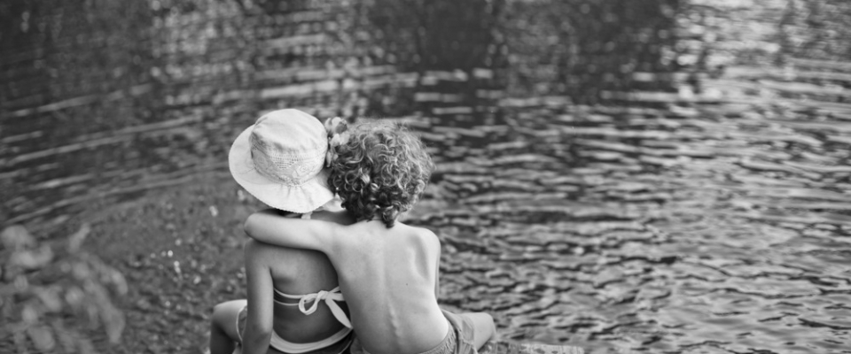 two children sitting on a jetty black and white